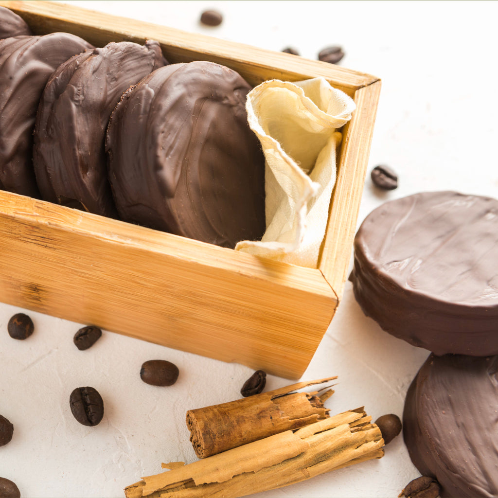 Chocolate-dipped Kunafa bites in a wooden box with coffee beans and cinnamon sticks on a white background